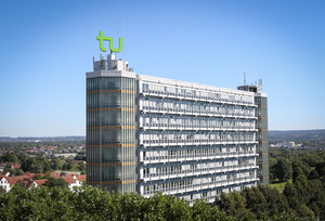 Mathematikgebäude mit Mathetower: Ein hohes Gebäude mit vielen Fenstern und je einem Turm an beiden Seiten. Auf dem linken Turm ein grünes TU-Logo. Im Hintergrund Häuser und Bäume.