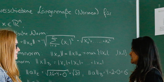 Studierende vor einer Tafel Zwei Studentinnen stehen vor einer Tafel und besprechen sich.